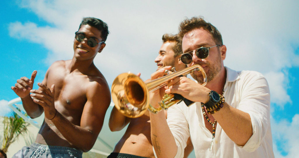 Men outdoors at a resort, one playing the trumpet