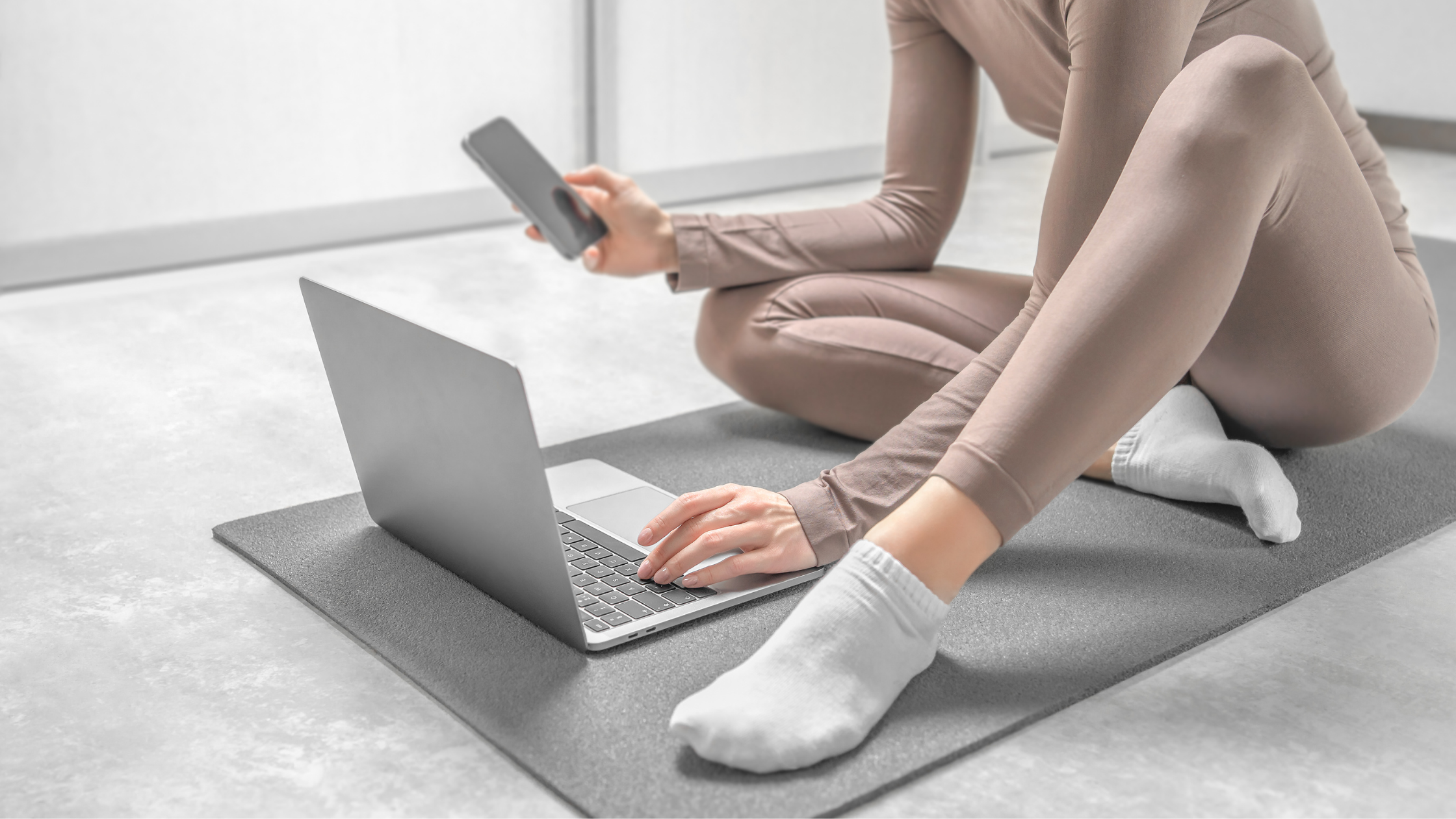 Person using their laptop and phone on a yoga mat