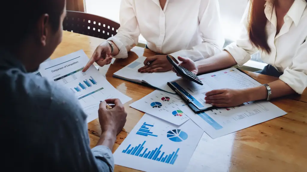 Three people around a table reviewing graphs and charts