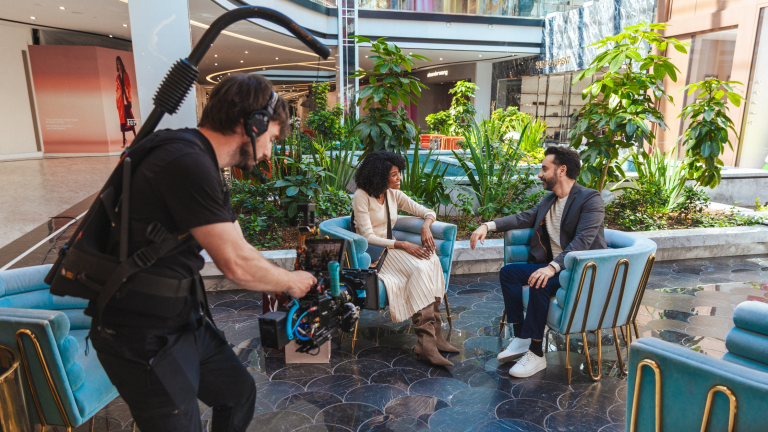 Video production crew member filming two people talking at a tourist destination